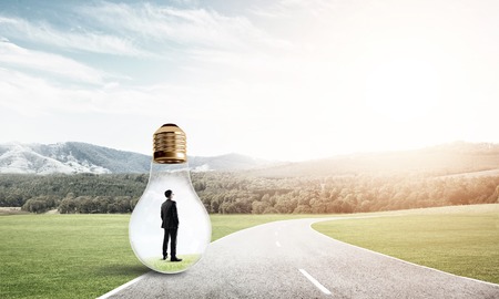 Young businessman trapped inside of light bulb on asphalt roadの写真素材