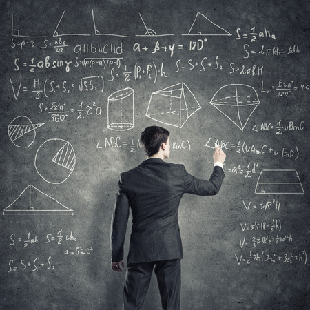 Man in suit standing with back and drawing formulas on chalkboardの写真素材
