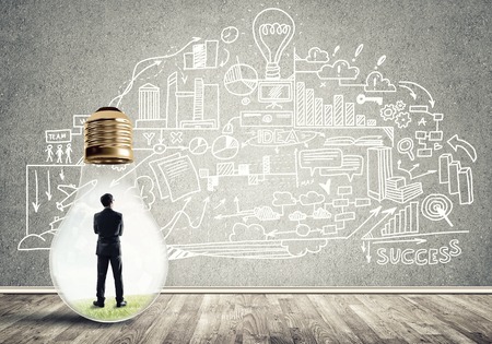 Businessman inside of light bulb in empty concrete room and sketches on wallの写真素材