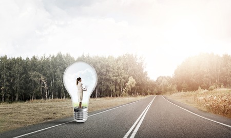 Young businesswoman trapped inside of light bulb on asphalt roadの写真素材