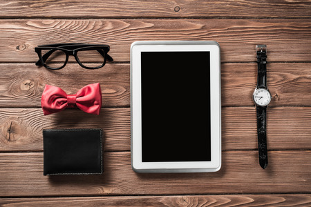Tablet pc computer wallet eyeglasses bowtie and wristwatch on tableの写真素材