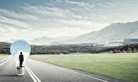 Young businessman trapped inside of light bulb on asphalt roadの写真素材