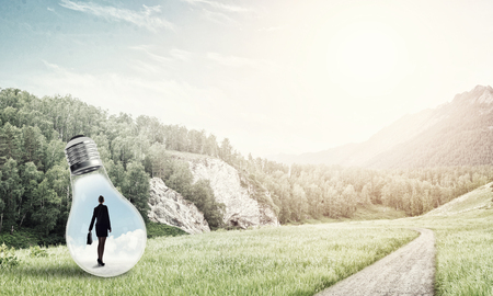 Young businesswoman trapped inside of light bulb on countryside roadの写真素材
