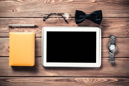Tablet pc computer wallet eyeglasses bowtie and wristwatch on tableの写真素材