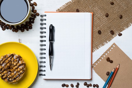 Opened notepad and cup of coffee with donut on wooden tableの写真素材