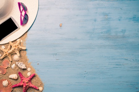 Straw hat sunglasses smartphone among sea shells and stones on wooden surfaceの写真素材