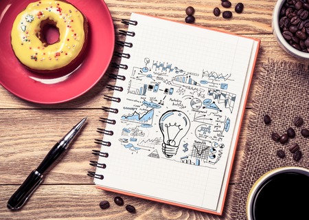 Notepad with idea sketches coffee cup and pencil on wooden tableの写真素材