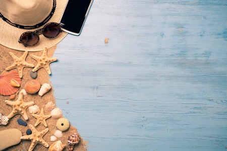 Straw hat sunglasses smartphone among sea shells and stones on wooden surfaceの写真素材