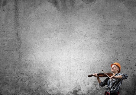 Engineer woman playing violin against concrete wall backgroundの写真素材
