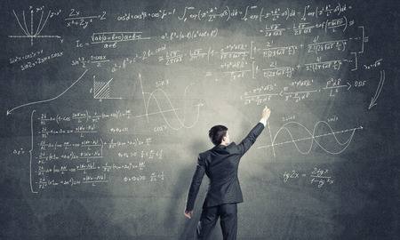 Man in suit standing with back and drawing formulas on chalkboardの写真素材
