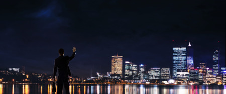 Elegant businessman with suitcase looking at night cityの写真素材