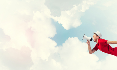 Young man shouting in megaphone with blue sky backgroundの写真素材