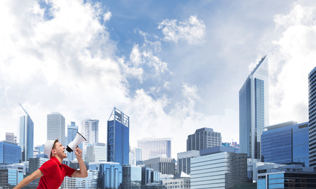 Young man against city background screaming emotional in megaphoneの写真素材