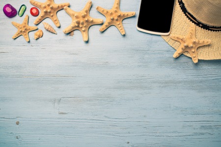 Straw hat sunglasses smartphone among sea shells and stones on wooden surfaceの写真素材