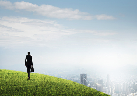 Businesswoman standing with back on top of hill and viewing modern cityの写真素材