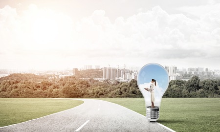 Young businesswoman trapped inside of light bulb on countryside roadの写真素材