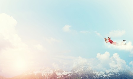 Young cheerful man flying high in sky and playing fifeの写真素材