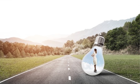 Young businesswoman trapped inside of light bulb on asphalt roadの写真素材