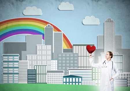 Young woman doctor against illustration background holding red heartの写真素材