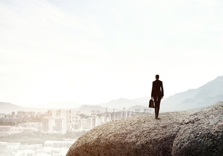 Businesswoman standing with back on top of hill and viewing modern cityの写真素材
