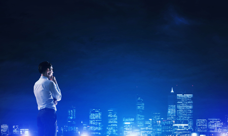 Elegant businessman with suitcase looking at night cityの写真素材
