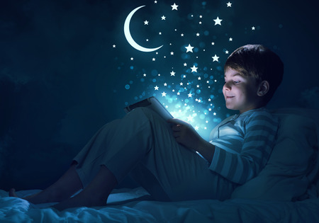 Teenage boy in pajamas lying in bed using tablet pc