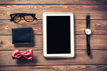 Tablet pc computer wallet eyeglasses bowtie and wristwatch on tableの写真素材