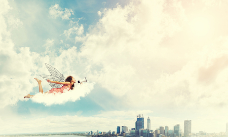 Young woman with megaphone flying high in skyの写真素材