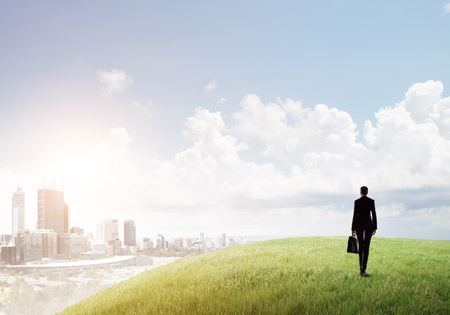 Businesswoman standing with back on top of hill and viewing modern cityの写真素材