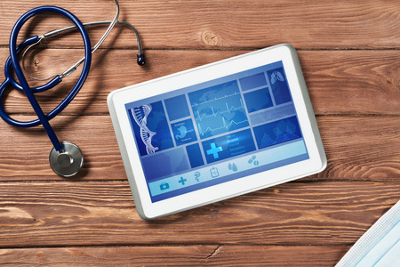 White tablet pc and doctor tools on wooden table