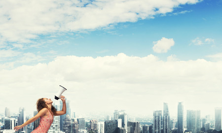 Young woman in dress making announcement in megaphoneの写真素材