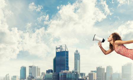Young woman in dress making announcement in megaphoneの写真素材