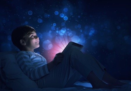 Teenage boy in pajamas lying in bed using tablet pcの写真素材