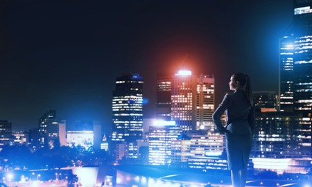 Rear view of elegant businesswoman viewing lights of night cityの写真素材