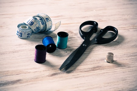 Old scissors bobbins threads and tape on wooden table