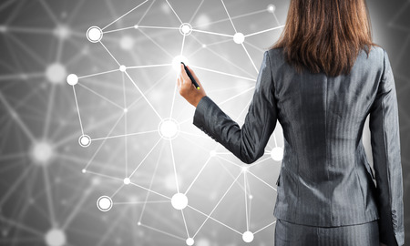 Businesswoman standing with back to camera and drawing with marker connection linesの写真素材