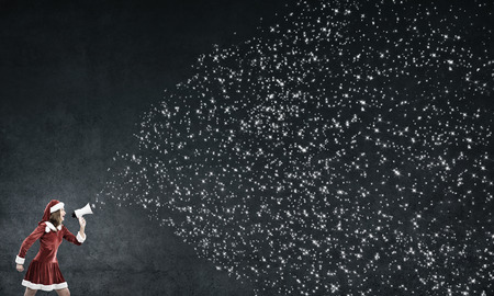 Attractive young woman in Santa suit making announcement in megaphoneの写真素材