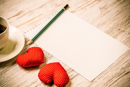 Coffee cup notepad pencil and two red hearts on wooden surfaceの写真素材