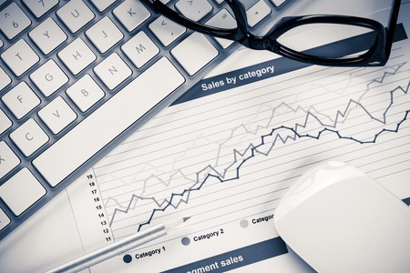 Business workplace with keyboard glasses and financial documents on tableの写真素材