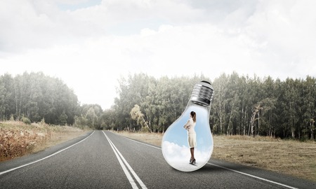 Young businesswoman trapped inside of light bulb on asphalt roadの写真素材