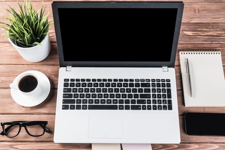 Still life photo of laptop notepad coffee glasses and other stuff on wooden tableの写真素材