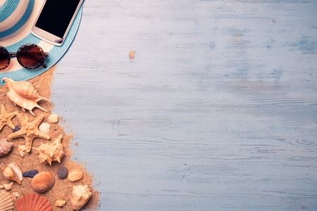Straw hat sunglasses smartphone among sea shells and stones on wooden surfaceの写真素材