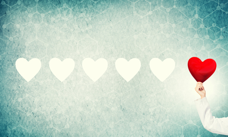 Hand of woman doctor against blue background holding red heartの写真素材