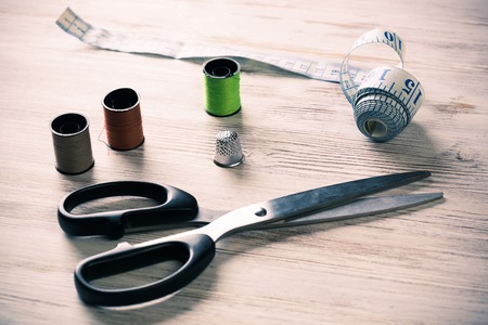 Old scissors bobbins threads and tape on wooden table