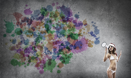 Attractive young woman in Santa hat and bikini making announcement in megaphoneの写真素材