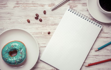 Opened notepad and cup of coffee with donut on wooden tableの写真素材