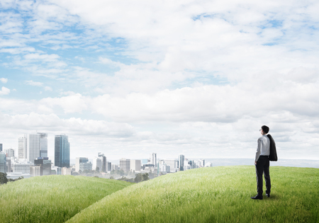 Businessman standing with back on top of hill and viewing modern cityの写真素材