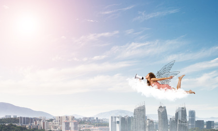 Young woman with megaphone flying high in skyの写真素材