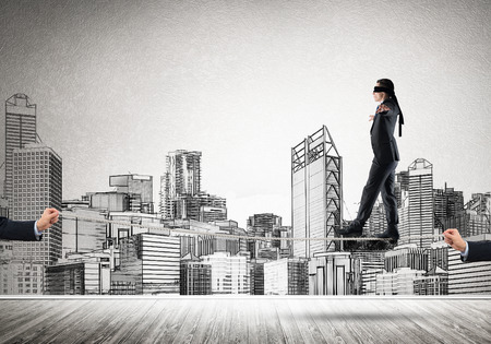 Businessman with blindfolder on eyes walking on ropeの写真素材