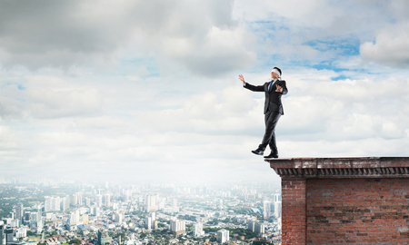 Businessman with blindfolder on eyes walking on building topの写真素材